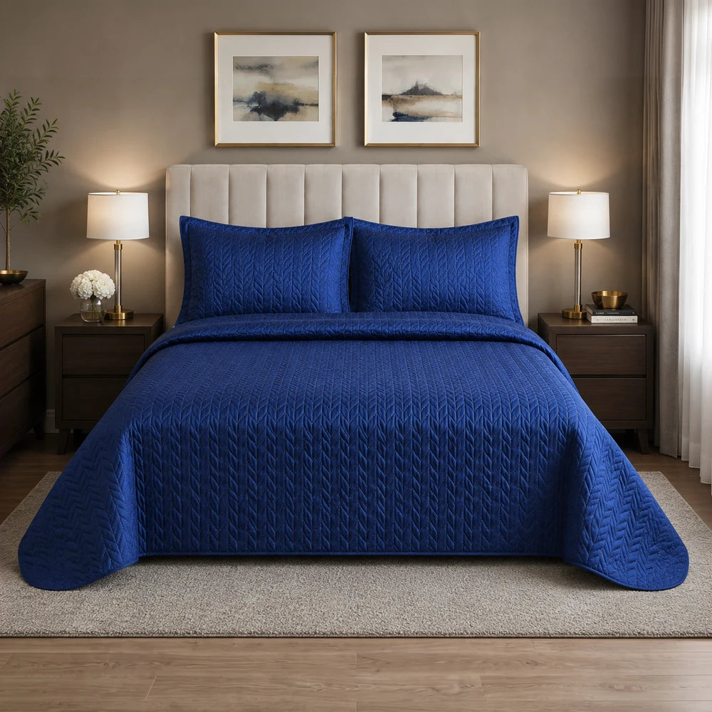 3Pc Ultrasonic Satin Quilt in deep blue with quilted chevron pattern and matching shams on a neatly made bed.