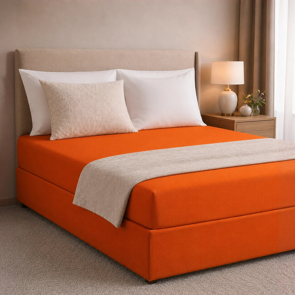 All-in-one Fitted Sheet and Base Cover in bright orange shown on a bed with white pillows and a beige decorative blanket.