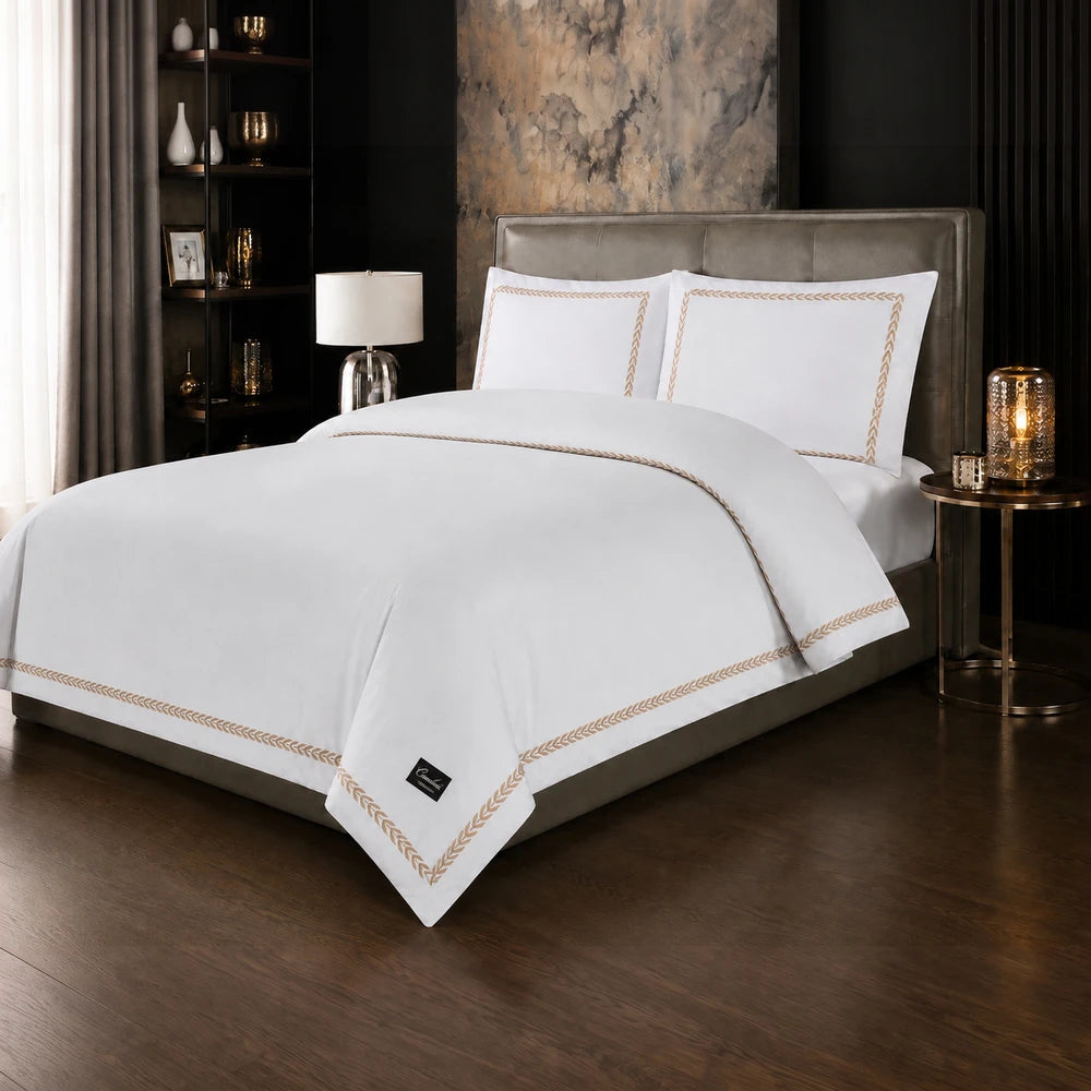 Carducci Serenity 100% cotton bedding in pure white with gold decorative trim, shown on a stylish bed with matching pillows.