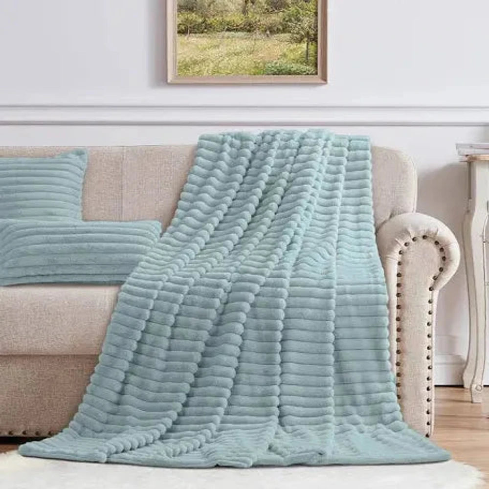 Cotton Co Faux Fur Milan Throw in light blue, a plush faux fur blanket draped over a beige sofa for cozy living room decor.