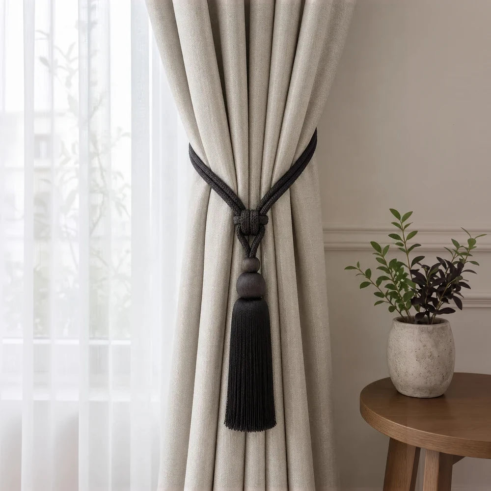 Curtain tieback with a black tassel knot securing beige curtains for a polished window look.