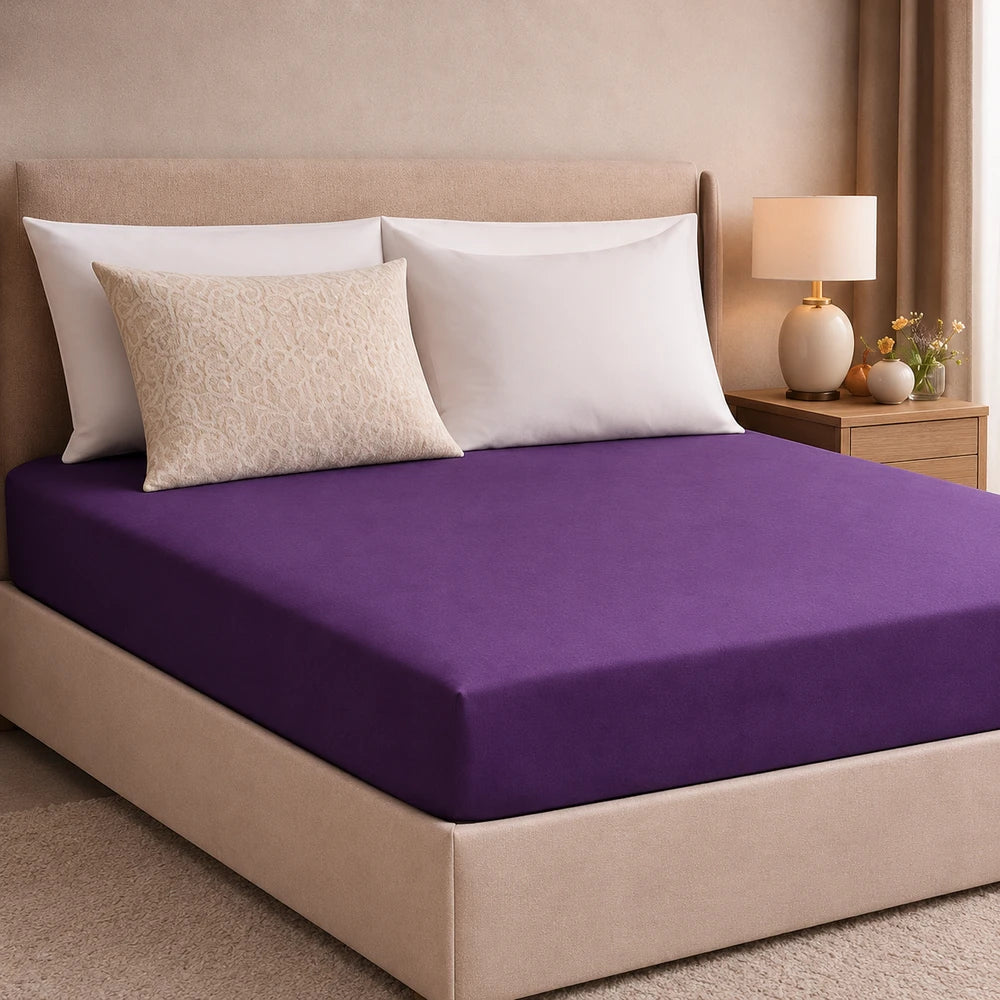 Plain microfibre fitted sheet in deep purple on a neatly made bed with white pillowcases and beige headboard.