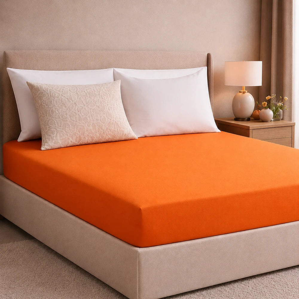 Plain microfibre fitted sheet in orange on a bed, highlighting its smooth fabric and snug fit.