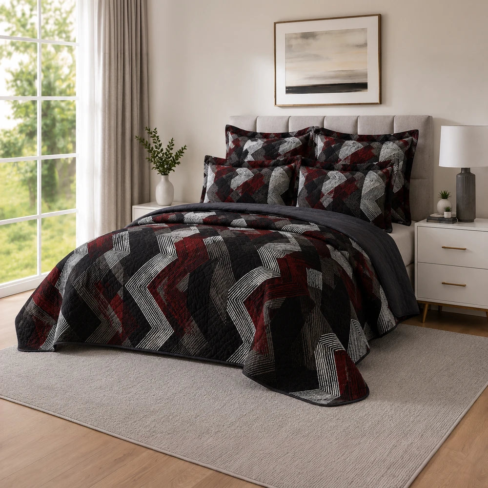 5PC Tela Milano quilt set in black, red, and gray geometric chevron pattern with matching shams on a cozy bed.
