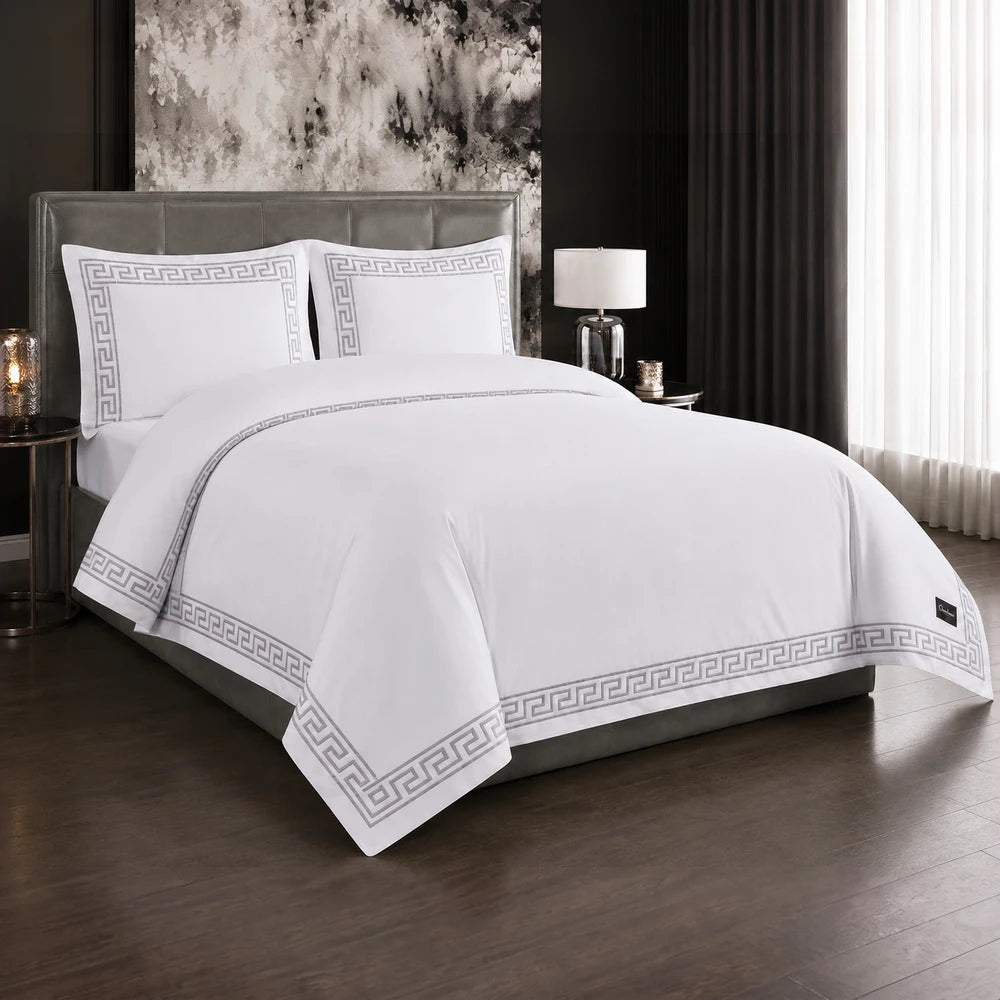 Carducci Odessa 100% cotton embroidered duvet cover in white with a grey Greek-key border, displayed on a bed.