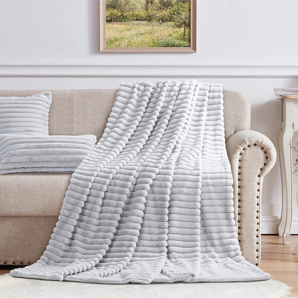 Cotton Co Faux Fur Milan Throw in light gray, plush blanket draped over a beige sofa for cozy, modern living room decor.