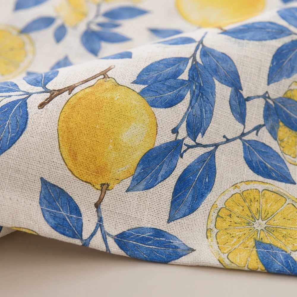 Linen look table cloth with yellow lemons and blue leaves on natural fabric, ideal for bright dining tables.