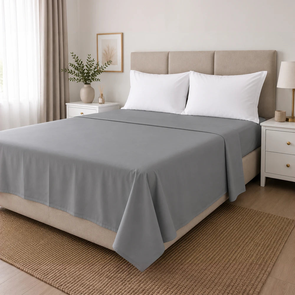 Microfibre flat sheet in soft gray draped over a neatly made bed with white pillows, showcasing smooth fabric and a calm