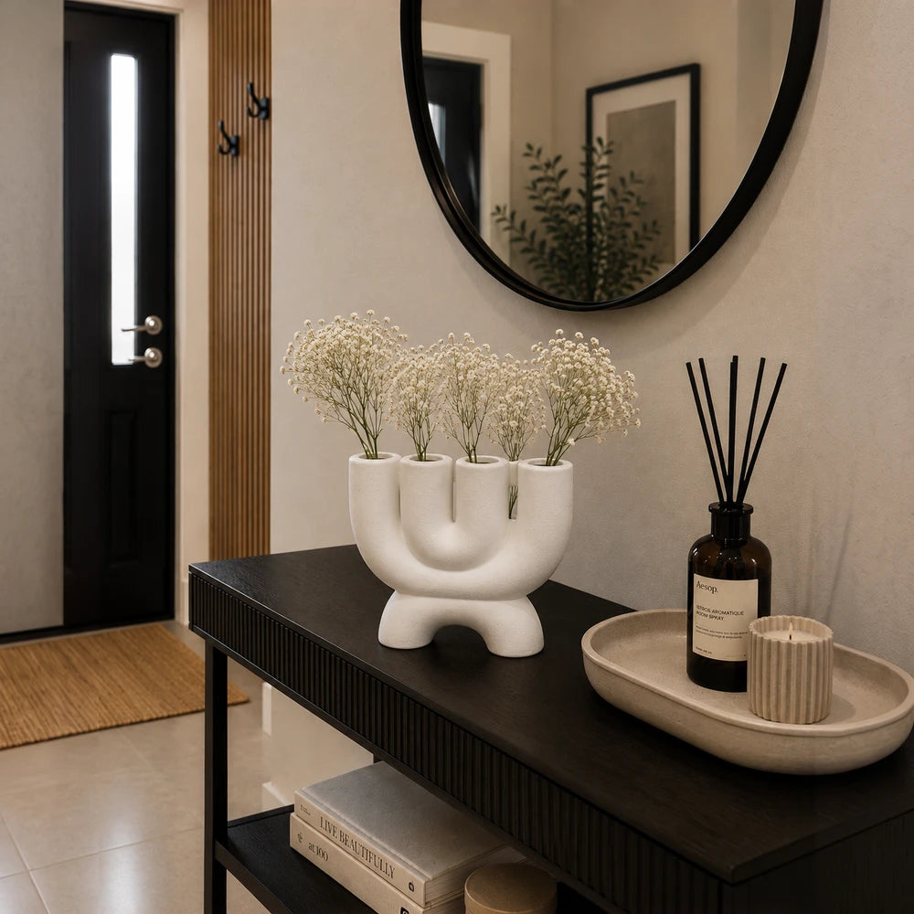 Modern white ceramic multi-opening vase with four vertical openings, displayed on a dark console table.