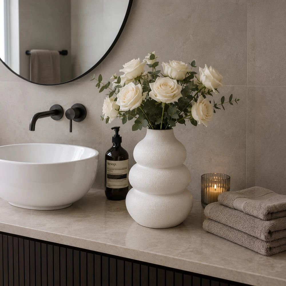 Modern white ceramic stacked pebble vase with white roses, decorative bathroom countertop.