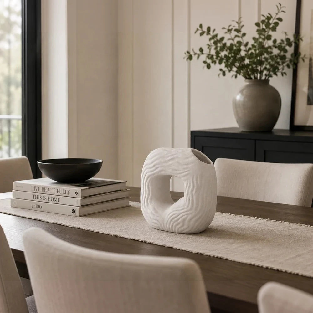 Modern white ceramic wavy donut vase with sculpted texture, shown on a dining table as a decorative centerpiece.