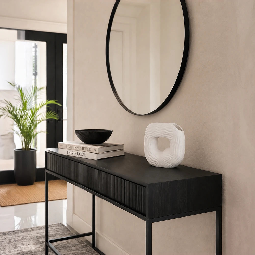 Modern white ceramic wavy donut vase displayed on a black console table with books in a contemporary entryway.