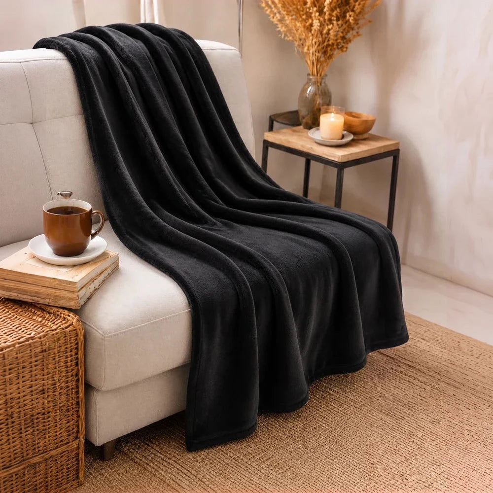 Pierre Cardin Classic Woven Throw in black, soft fleece fabric draped over a beige sofa for cozy evenings.