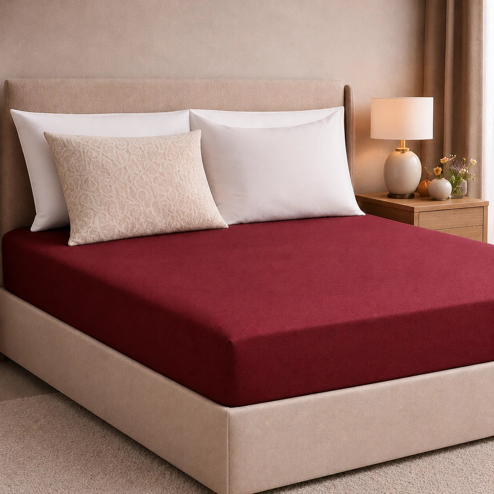 Plain Microfibre Fitted Sheet in burgundy on a bed with a beige headboard and white pillows for a cozy bedroom look.