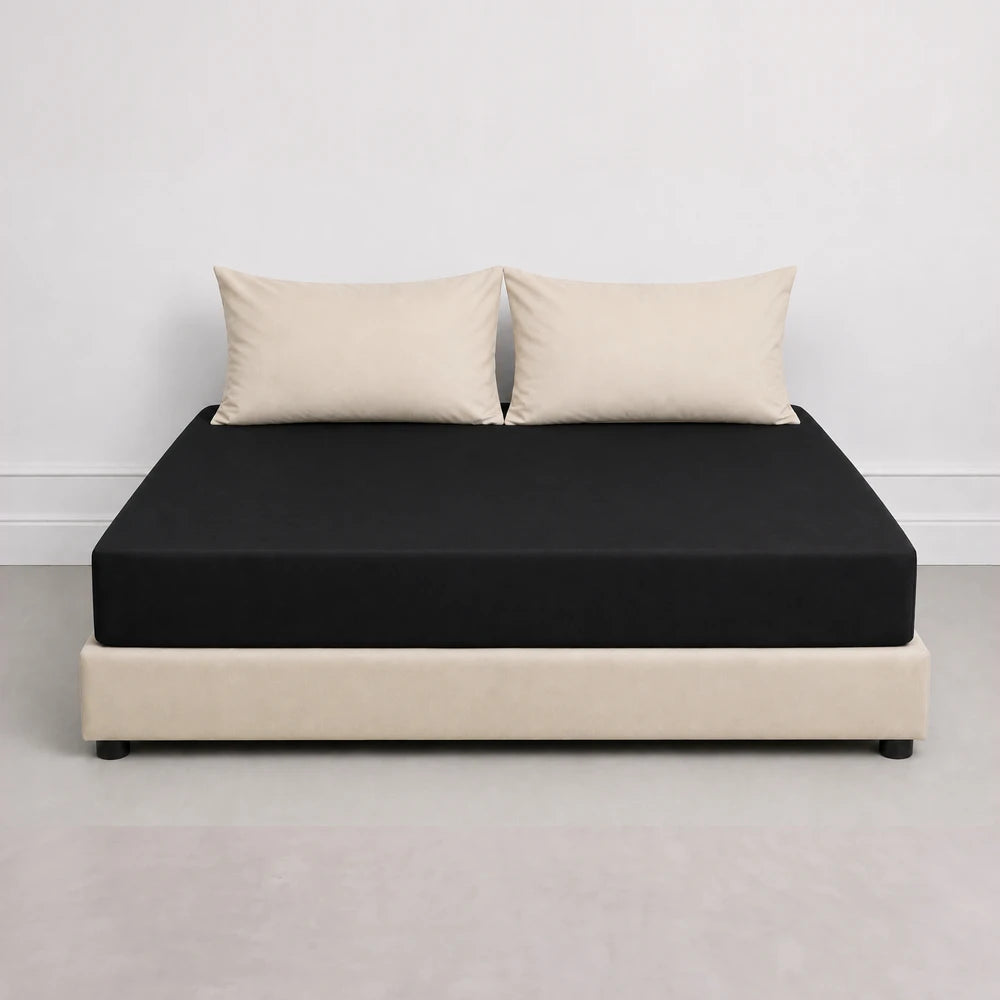 Whisper Soft Microfibre Fitted Sheet in black on a bed, paired with beige pillows; smooth, secure-fit fabric.