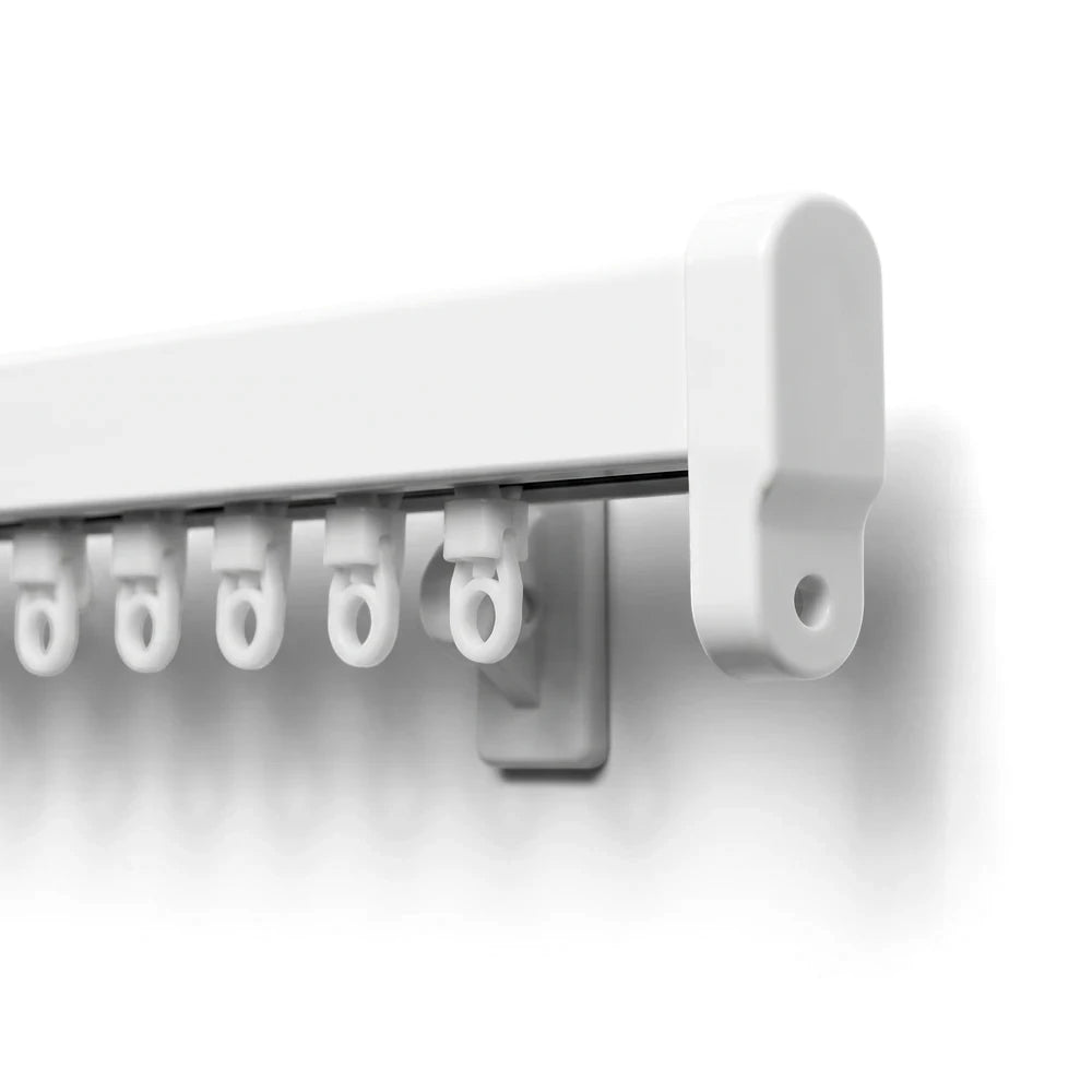 Close-up of a white curtain track system featuring multiple C-shaped hangers and an end cap, mounted on a plain wall.